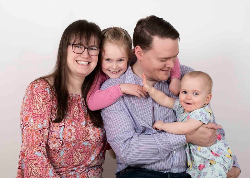 Mum, Dad and two daughters cuddled together smiling at camera and each other